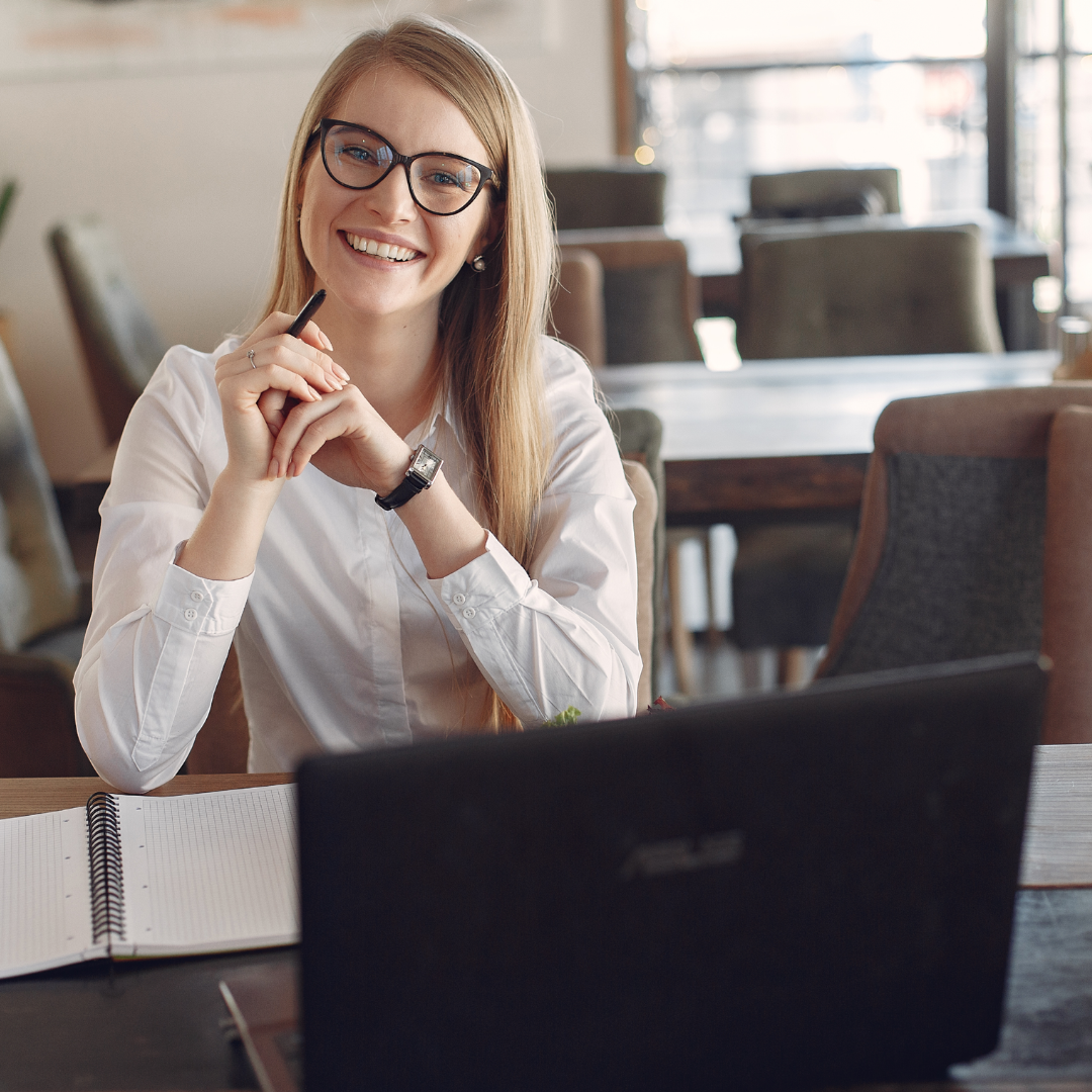 Contadora sorrindo durante atendimento, com notebook e caderno sobre a mesa